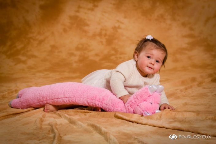 Portrait de bébé avec doudou rose sur fond brun